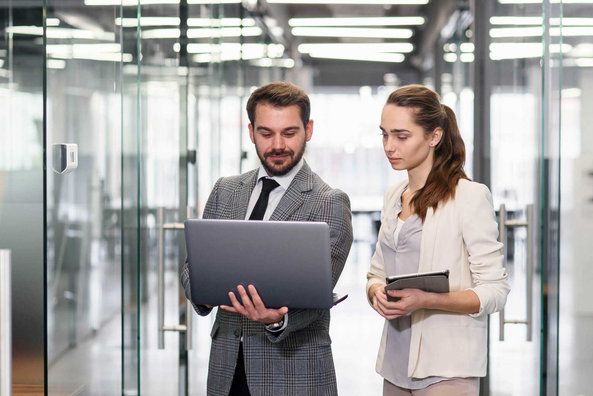Geschäftsmann und Geschäftsfrau mit Laptop stehen in einem leeren Büroflur und besprechen ein neues Projekt.